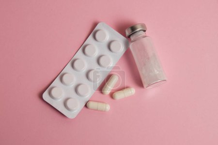 Foto de White medical capsules, ampoule and pills in blister pack on pink paper background - Imagen libre de derechos