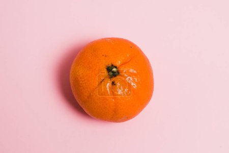 One tangerine on a pink paper background with copy space