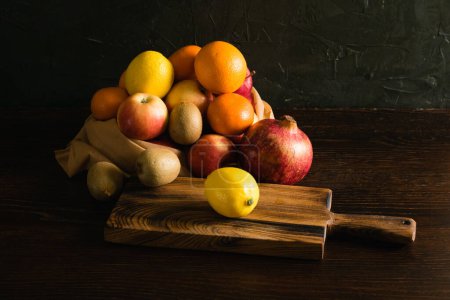 Téléchargez les photos : Fruits dans un sac réutilisable. Jour de la Terre et concept zéro déchet. Orange, citron, pomme, kiwi, grenade et planche à découper en bois sur fond sombre. - en image libre de droit