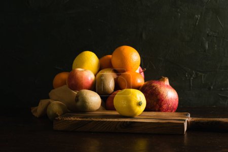 Téléchargez les photos : Fruits dans un sac réutilisable. Jour de la Terre et concept zéro déchet. Orange, citron, pomme, kiwi, grenade et planche à découper en bois sur fond sombre. - en image libre de droit