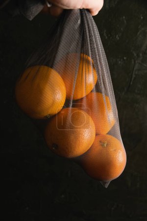 Téléchargez les photos : Concept de jour de la terre, compostage, zéro déchet et recyclage. Oranges dans un filet réutilisable pour acheter des légumes et des fruits sur un fond sombre. - en image libre de droit