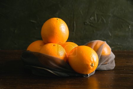 Téléchargez les photos : Concept de jour de la terre, compostage, zéro déchet et recyclage. Oranges dans un filet réutilisable pour acheter des légumes et des fruits sur un fond sombre. - en image libre de droit