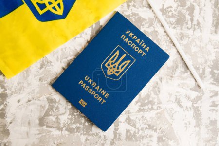 Flatlay, Ukrainian passport and flag on light concrete background with copy space.