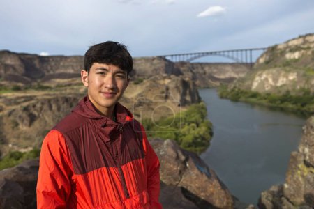 Téléchargez les photos : Un adolescent se tient sur des rochers plus élevés avec le pont Perrine et Snake RIver derrière lui à Twin Falls, Idaho. - en image libre de droit
