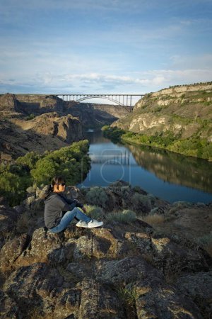 Téléchargez les photos : Une femme est assise sur un rocher profitant du paysage le long de la rivière Snake et du pont Perine à Twin Falls, Idaho. - en image libre de droit