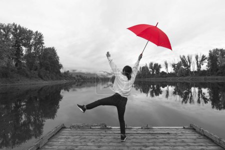 Photo for A concept digitally enhanced photo of a black and white photo of a woman standing on a dock holding a red umbrella by the Kootenai River in North Idaho. - Royalty Free Image