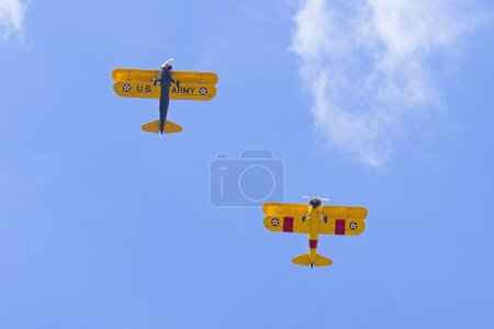 Two old style biplanes fly directly over head in the bright blue sky near Liberty Lake, Washington.