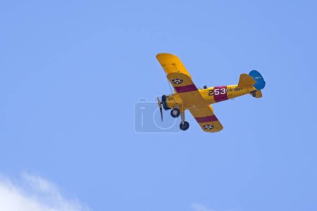 A yellow old style biplane soars up in the bright blue sky near Liberty Lake, Washington.
