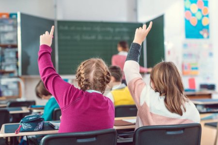 Two girl students raising hands to answer a question in school class because they know the answer