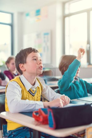 Photo for Boy student in class of elementary school knowing an answer raising his hand - Royalty Free Image