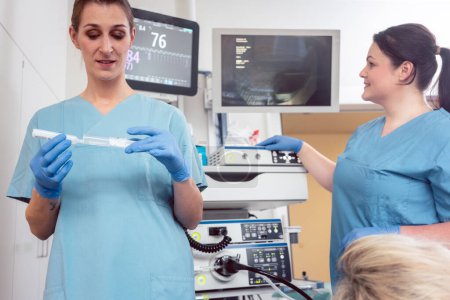 Foto de Enfermera preparando anestésico para cirugía en hospital, paciente y segunda enfermera en segundo plano - Imagen libre de derechos