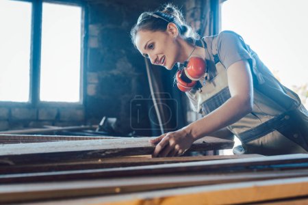 Téléchargez les photos : Femme charpentier choisissant le bois dans son rangement pour le prochain projet - en image libre de droit