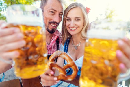 Téléchargez les photos : Couple toasting à la caméra dans le jardin de la bière bavaroise - en image libre de droit