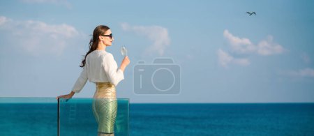 Téléchargez les photos : Femme dégustant une coupe de champagne à la mer debout sur la terrasse de la maison de plage - en image libre de droit