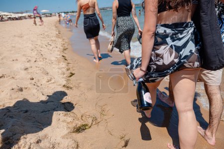 Téléchargez les photos : Quatre jeunes marchant sur la plage avec bouteille de champagne - en image libre de droit
