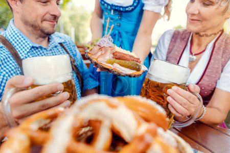 Téléchargez les photos : Serveur apportant de la nourriture à coupler dans un jardin de bière avec des bretzels au premier plan - en image libre de droit