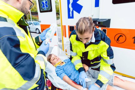 Foto de Médicos de emergencia poniendo niño herido en coche ambulancia - Imagen libre de derechos