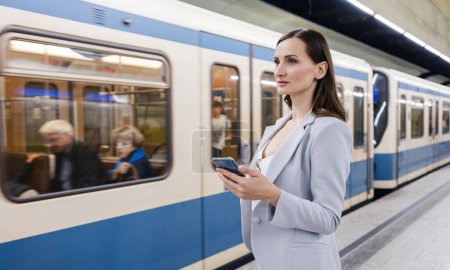 Foto de Mujer de traje con teléfono en la mano en la estación de metro con tren llegando - Imagen libre de derechos