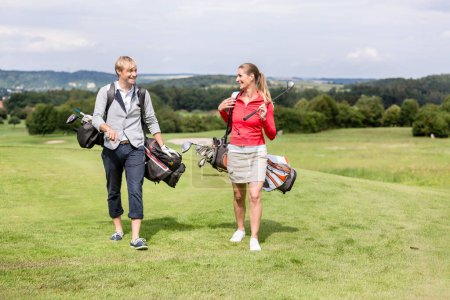 Photo for Happy young golfing couple walking with shoulder bag on course - Royalty Free Image