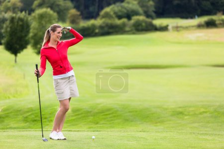 Photo for Smiling attractive female golfer shielding eyes while standing on field - Royalty Free Image
