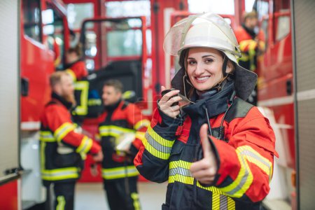 Foto de Hermosa mujer bombero con su casco en la mano de pie en la estación de bomberos - Imagen libre de derechos