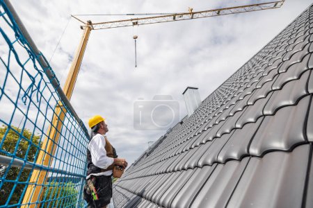 Téléchargez les photos : Toiture debout sur l'échafaudage sur le chantier de construction grue de fonctionnement à l'aide de la télécommande - en image libre de droit