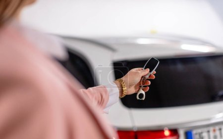 Téléchargez les photos : Femme utilisant un fob comme clé pour ouvrir sa voiture de la classe moyenne supérieure dans le garage - en image libre de droit