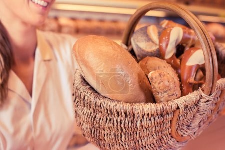 Foto de Mujer de ventas en panadería presentando una canasta con pan y panecillos - Imagen libre de derechos