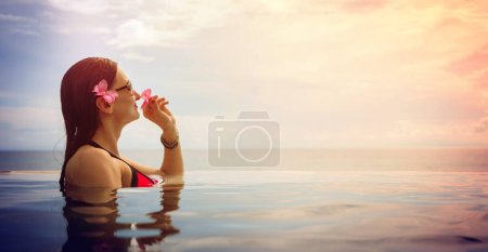 Photo for Beautiful woman in an infinity pool in front of the sea enjoying a tropical vacation watching the sunset - Royalty Free Image