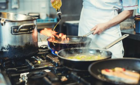 Photo for Chef with pans on the stove cooking in a restaurant kitchen with olive oil - Royalty Free Image