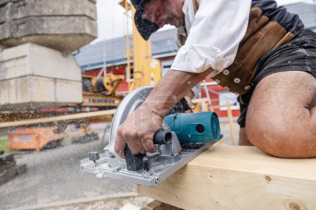 Foto de Carpintero en un sitio de construcción que corta una viga de madera con una sierra eléctrica - Imagen libre de derechos