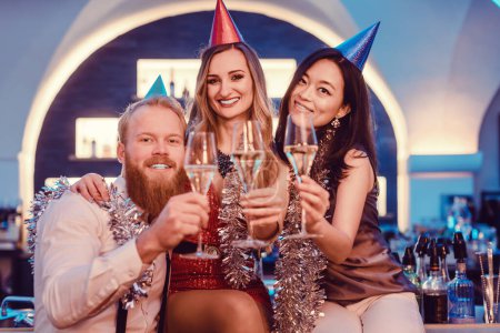 Photo for Smiling multiracial friends holding champagne flute in hand posing in nightclub - Royalty Free Image