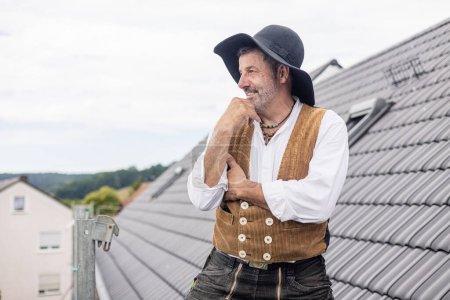 Photo for Roofer in traditional gear standing on roof of residential home looking proud - Royalty Free Image