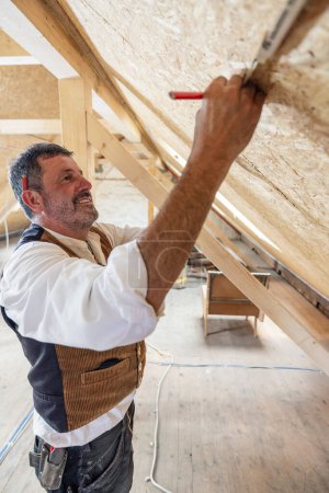 Téléchargez les photos : Travailleur du bois de construction mesurant sur place la conversion des greniers - en image libre de droit