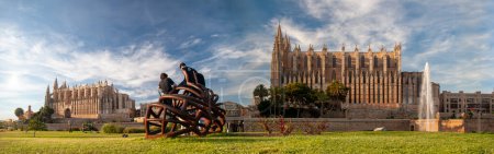 Photo for An alternative panoramic image of Palma de Mallorca's Cathedral, depicted twice from different angles. Dominated by a foreground of green grass with three individuals on a metal ornament, under a partially clouded blue sky - Royalty Free Image