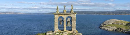 Photo for An ancient bell tower rises as a solitary sentinel on the edge of a cliff, its weathered stones and aged bells facing the endless blue sea. This historic watchtower offers a commanding view of the rugged coastline and distant hills, under the expansi - Royalty Free Image