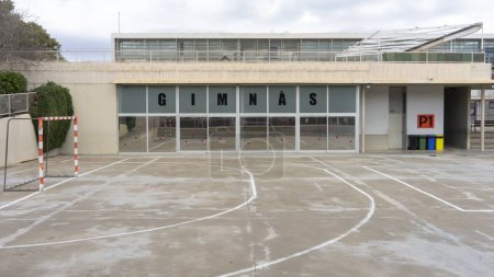 Foto de Una cancha deportiva al aire libre vacía espera a los jugadores, con una gran fachada de cristal de gimnasios que refleja el cielo abierto en Mallorca - Imagen libre de derechos