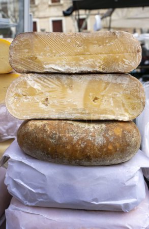 Three mature cheese wheels, showcasing the art of traditional cheese-making, are stacked, ready to entice gourmands at a local market.