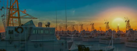 Téléchargez les photos : Un coucher de soleil éclatant enveloppe les navires de la Garde côtière dans un port, irradiant un spectre de teintes chaudes. - en image libre de droit