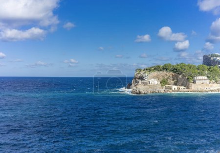 Foto de El icónico faro de Port de Sóller hace guardia en el acantilado rocoso, un faro contra el profundo mar azul y el cielo. - Imagen libre de derechos