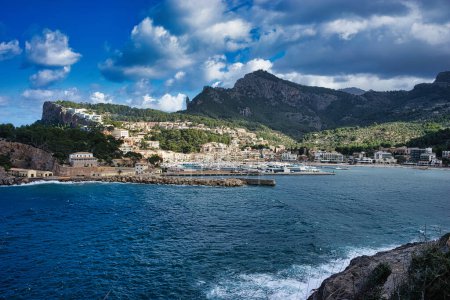 A bustling port town of Soller nestled between verdant mountains and the deep blue sea, under the watchful eye of white clouds.