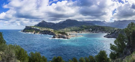 A broad panoramic shot featuring the dynamic coastline of Port de Soller, cliffside structures, and the Serra de Tramuntana.