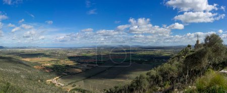 Faszinierende Weitwinkelkulisse der mallorquinischen Landschaft mit einem Steinkreuz auf einem Hügel vor einem dynamischen Himmel.