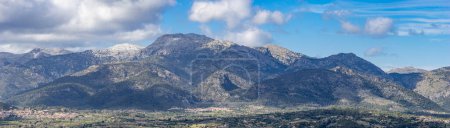 The Tramuntana Range stands grand, overlooking the serene landscape of Mallorca under a cloudy sky.