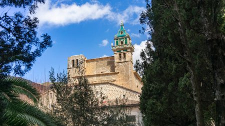 Antiguo Monasterio Cartujo con distintiva aguja de azulejos verdes y ocres abrazada por un exuberante follaje.