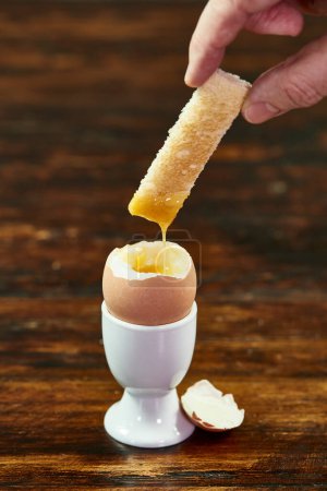 Hand Dipping a Soldier Toast Into a Soft-Boiled Egg in a White Eggcup