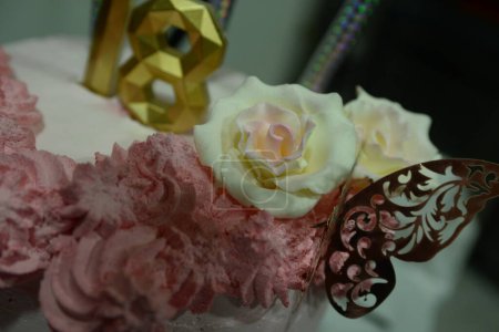 Téléchargez les photos : Gros plan de gâteau rose blanc avec des fleurs rose foncé en remplissage, décoration papillon, feux d'artifice et bougie dorée en forme de numéro 18 - en image libre de droit