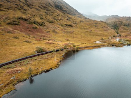 Téléchargez les photos : Train à vapeur passant par un loch et des montagnes à l'automne - en image libre de droit