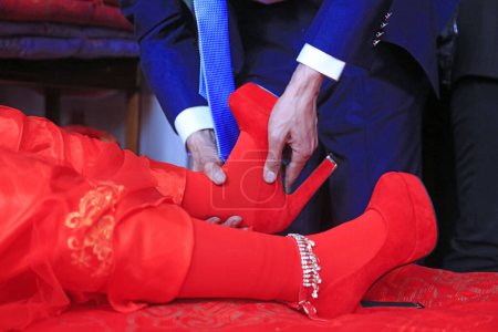 Téléchargez les photos : Cérémonie de mariage chinoise, marié porte des chaussures pour mariée - en image libre de droit