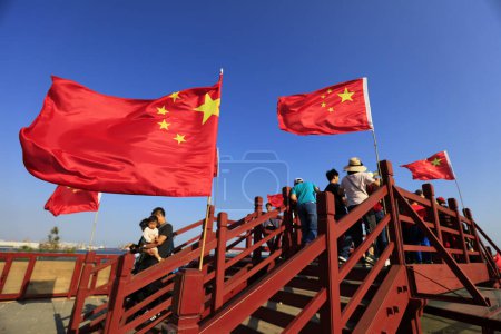 Foto de Ciudad de Qinhuangdao, China - 4 de octubre de 2018: Los turistas caminan a través del antiguo lugar escénico de la cabeza del dragón en el caballete lleno de banderas rojas, Ciudad de Qinhuangdao, provincia de Hebei, China - Imagen libre de derechos